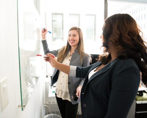two women in front of dry erase board