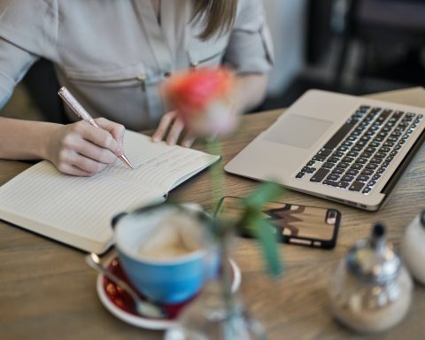 person writing on a notebook beside macbook