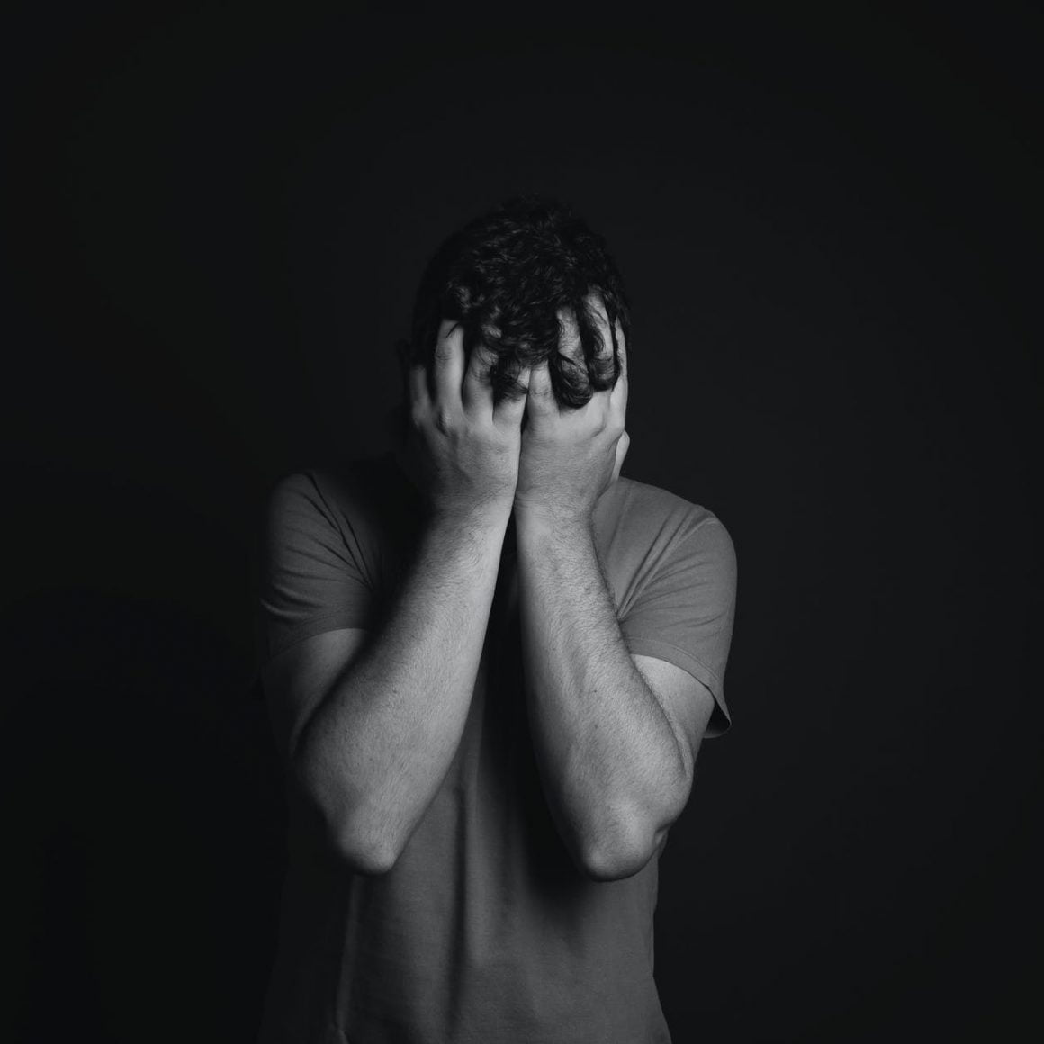 gray scale photo of man covering face with his hands