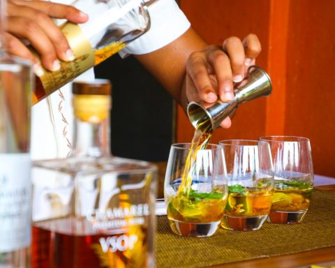 person poring cocktail on clear drinking glass