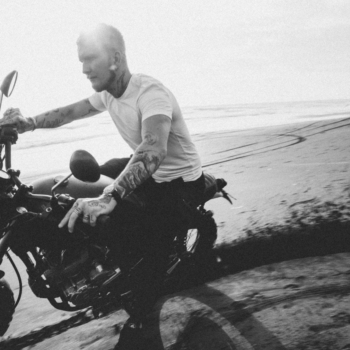 tattooed motorcyclist riding bike on sandy beach near ocean