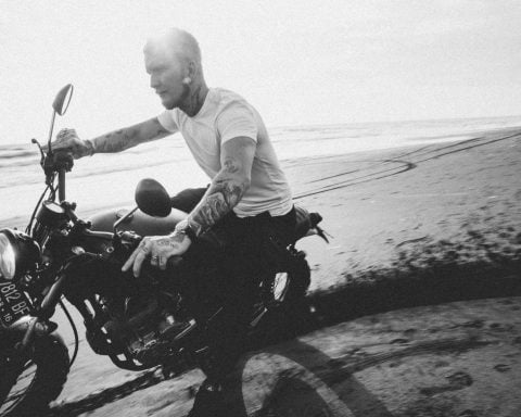 tattooed motorcyclist riding bike on sandy beach near ocean