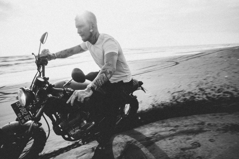 tattooed motorcyclist riding bike on sandy beach near ocean