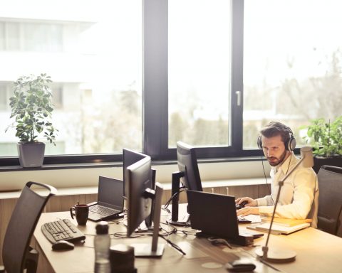 man with headphones facing computer monitor