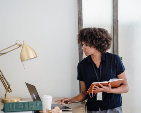 woman holding a notebook and using a laptop
