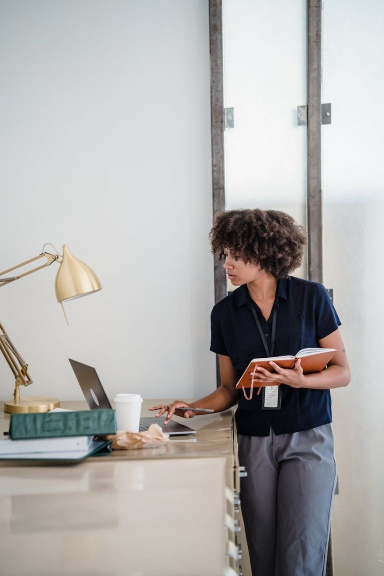 woman holding a notebook and using a laptop