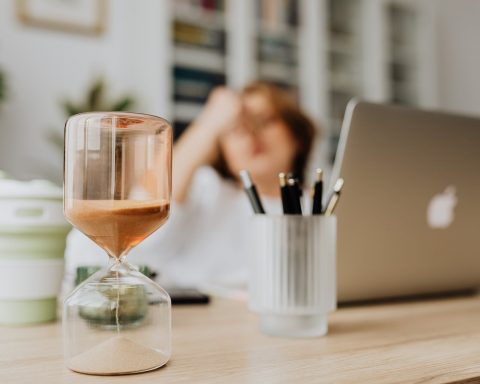 hourglass on a desk of a woman sitting in front of her laptop