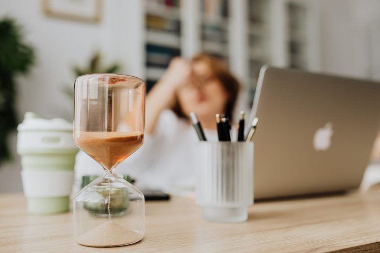 hourglass on a desk of a woman sitting in front of her laptop