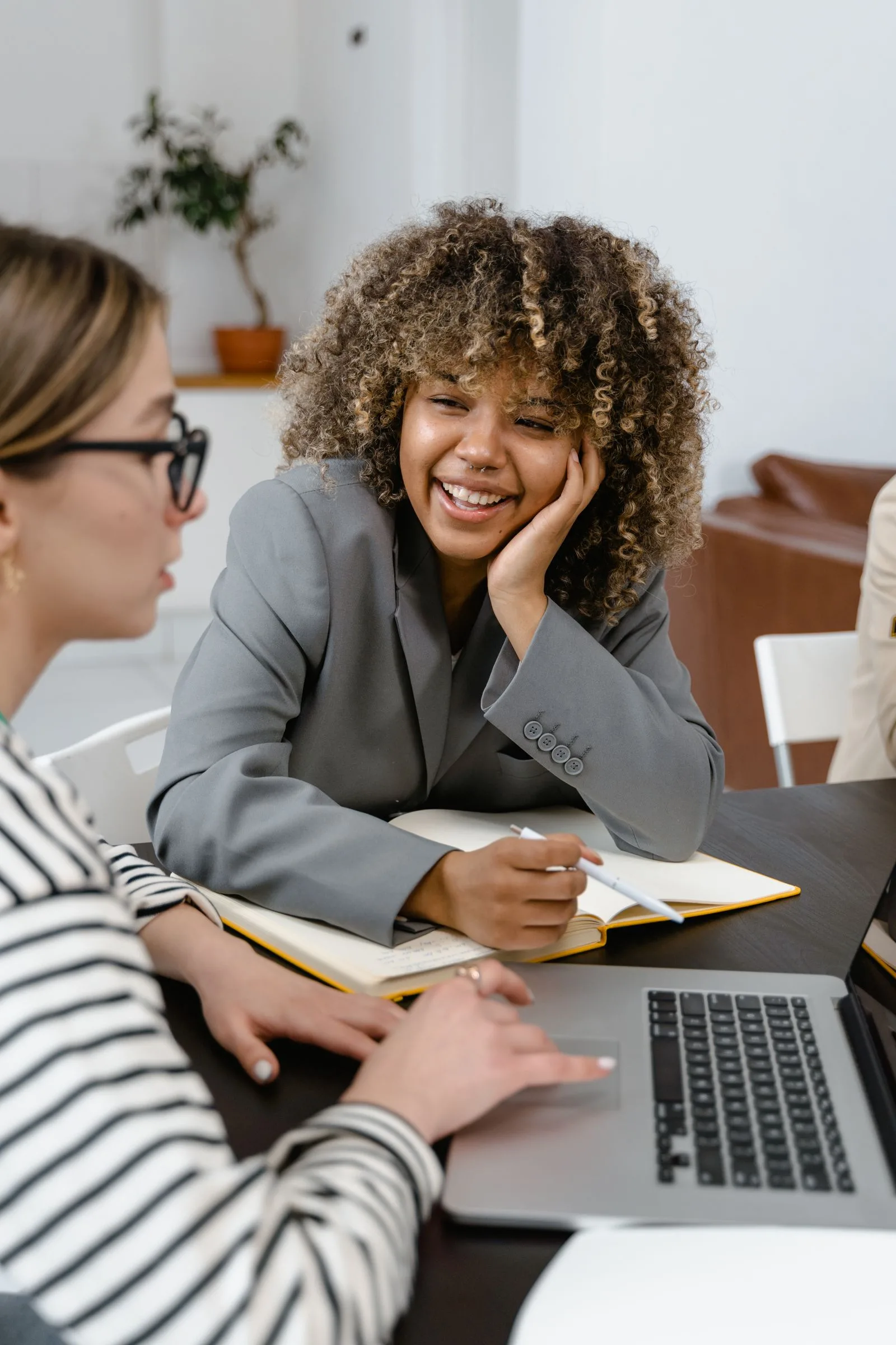 Vrouw in grijze blazer kijkt glimlachend mee naar het werk van een collega achter een laptop op kantoor
